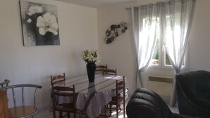 A dining area with a round table, chairs, a vase with flowers, a painting on the wall, and a window with curtains. - charming holiday home, Bourcefranc le chapus (Bourcefranc-Le-Chapus)
