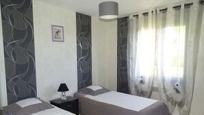 A bedroom with two single beds, a nightstand with a lamp, a large window with sheer curtains, and a wall with abstract designs. - charming holiday home, Bourcefranc le chapus (Bourcefranc-Le-Chapus)