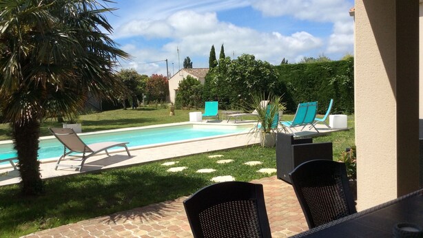 A pool area with lounge chairs and a table, surrounded by greenery and a clear sky. - charming holiday home, Bourcefranc le chapus (Bourcefranc-Le-Chapus)
