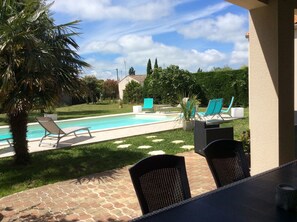 Un área de piscina con sillones de descanso y una mesa, rodeada de vegetación y un cielo despejado.