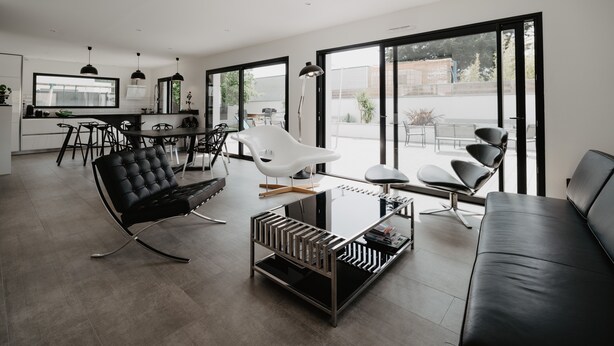 Un salon moderne avec un canapé en cuir noir, une table basse en verre et des fauteuils contemporains.
