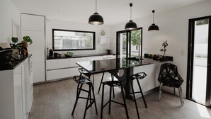 Une cuisine moderne avec des meubles blancs, des tabourets de bar noirs et des luminaires suspendus.