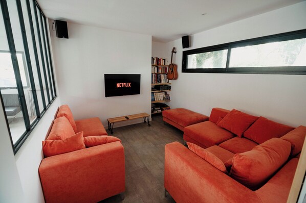 Una sala de estar moderna con sofás naranjas, un televisor de pantalla plana, una estantería y una guitarra.