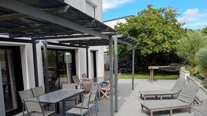 Une terrasse extérieure dotée d’une pergola, d’une table à manger avec des chaises, et de fauteuils de relaxation.