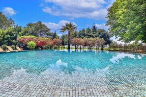 Una piscina azul cristalina con bordes de azulejos, rodeada de exuberante vegetación y árboles.