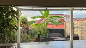 A covered outdoor seating area with a view of a red-roofed building, surrounded by lush greenery. - Pleasant apartment. on the ground floor 5 mins walk from the beach, Sainte Anne (SAINTE ANNE)