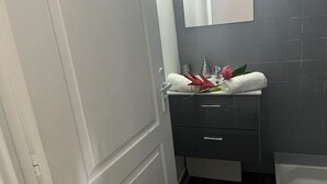 A bathroom with a white door, a mirror, a sink with a white countertop, and a towel rack with a red towel and a pink flower. - Pleasant apartment. on the ground floor 5 mins walk from the beach, Sainte Anne (SAINTE ANNE)