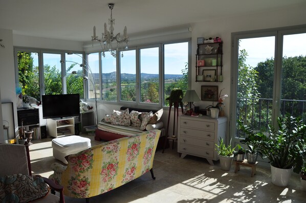 A spacious living room with a large window, a sofa, a television, and various decorative items.