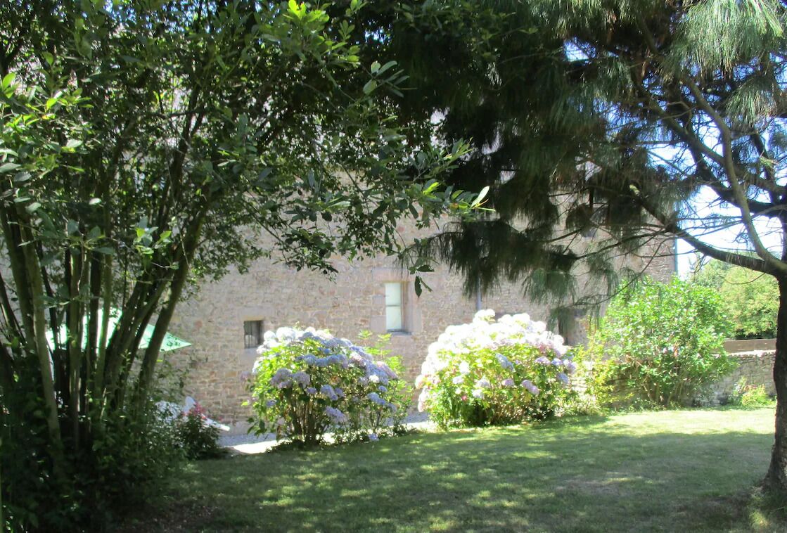 A stone building with a garden in front, surrounded by trees.