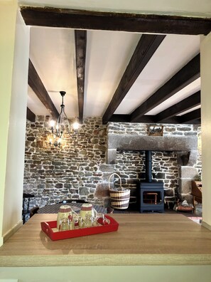 Un intérieur rustique avec des poutres apparentes, un mur en pierre, une cheminée et une table en bois sur laquelle est posée une corbeille de verres.