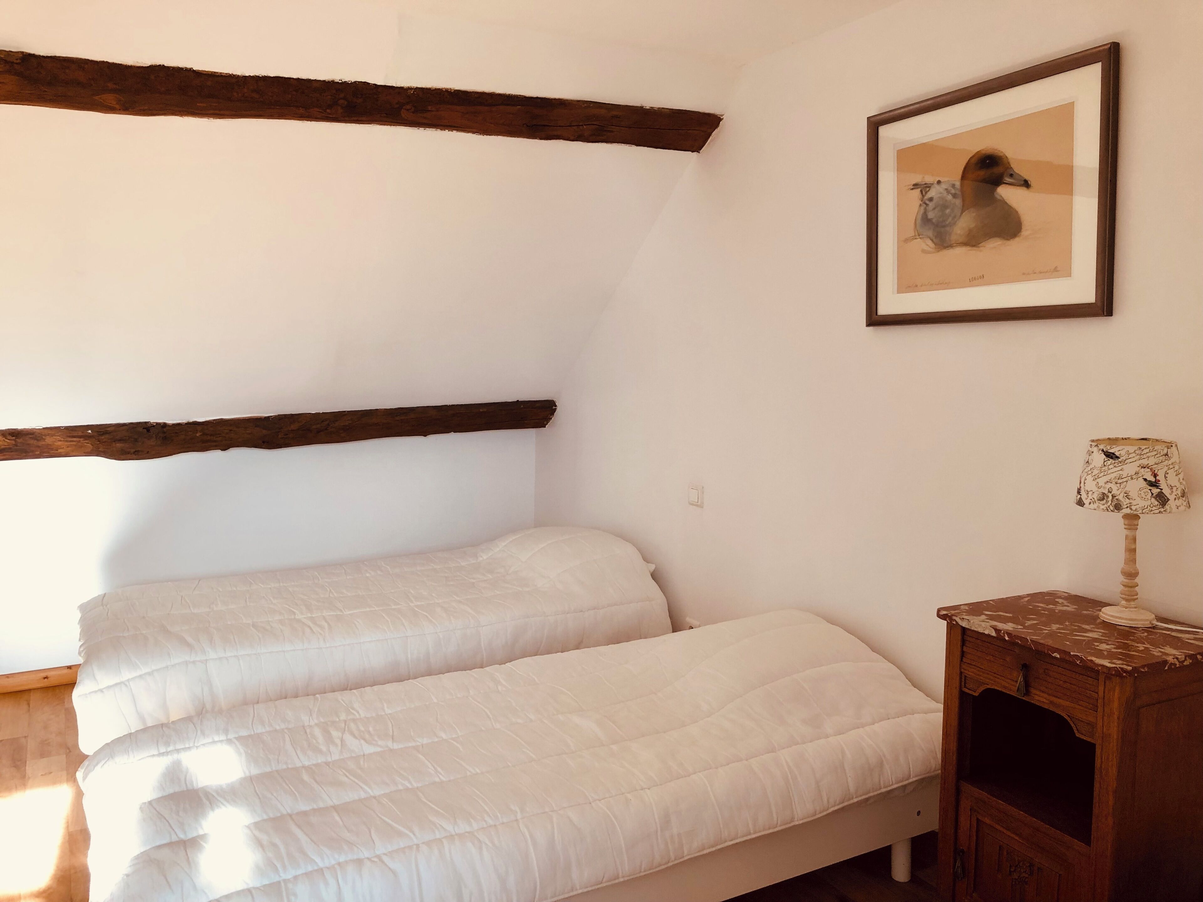 Et soveværelse med en seng, et træhovedgærde, et billede i ramme på væggen og et sengebord med en lampe.