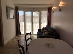 A dining area with a round table, chairs, a sofa, and a sliding glass door leading to a balcony.