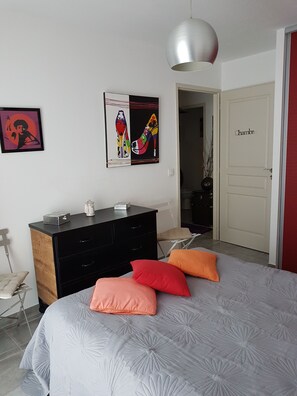 Ein Schlafzimmer mit einem Bett, einem Schminktisch, einer Tür mit der Aufschrift 'Chamb' und einer Wand mit zwei Kunstwerken.