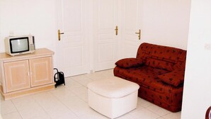A room with a television on a cabinet, a red patterned sofa, and a white ottoman. - BEAUTIFUL APARTMENT FOR 4 PEOPLE WELL (Propriano)