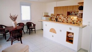 A compact kitchen with wooden cabinets, a tiled backsplash, and a small island. There is a dining area with a table and chairs, and a vase with flowers on the table. - BEAUTIFUL APARTMENT FOR 4 PEOPLE WELL (Propriano)