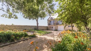 A garden with a variety of plants and flowers, a stone wall, and a building with a garage. - Beautiful house with sea view and fireplace (Ver-sur-Mer)