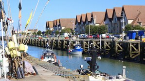 A marina with boats docked, a wooden pier, and residential buildings in the background. - Beautiful house with sea view and fireplace (Ver-sur-Mer)