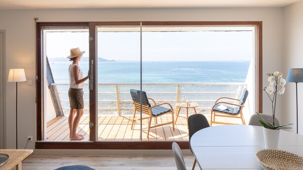 Une pièce dotée d’une grande porte-fenêtre coulissante qui donne sur un balcon offrant une vue sur l’océan. On y trouve deux chaises et une petite table.