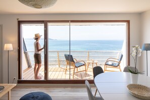 Ein Zimmer mit einer großen Schiebetür, die auf einen Balkon mit Meerblick führt. Auf dem Balkon befinden sich zwei Stühle und ein kleiner Tisch.