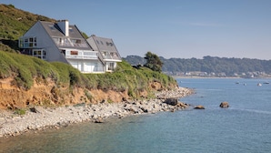 Une maison située sur la côte, dotée d’un toit en pente, de grandes fenêtres et d’un balcon offrant une vue sur la mer.