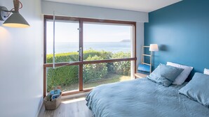 Une chambre avec une grande fenêtre, un lit avec une literie bleue et une vue sur la mer.