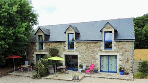 A stone house with a gravel driveway, outdoor seating, and a large tree to the left. - cottage swallows (Riec-sur-Bélon)