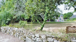 A stone wall with a bench, a pond, and a house in the background. - cottage swallows (Riec-sur-Bélon)