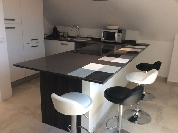 A modern kitchen with a central island, bar stools, a microwave, and a sink.