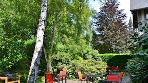 An outdoor seating area with tables and chairs, surrounded by lush greenery and trees.