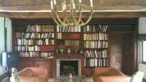 A cozy living room with a fireplace, two armchairs, and a bookshelf filled with books.