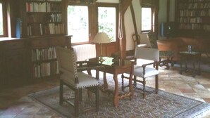 A cozy library with bookshelves, a wooden table with chairs, and a patterned rug.