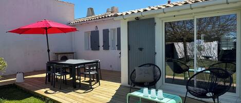 Un patio con una mesa y sillas, una sombrilla roja y una mesita con tazas.