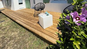 A white building with green shutters, a wooden deck, and a white table with chairs.