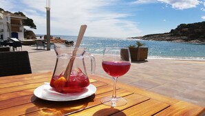 A table with a pitcher and a wine glass, a wooden bench, and a view of the sea and buildings. - Architect- villa, heated infinity pool, stunning 360° sea/mountain view, WIFI (Tamariu)