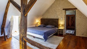 Een slaapkamer met een schuine kap, een bed met een donker hoofdeinde, twee bedlampen en een houten vloer.