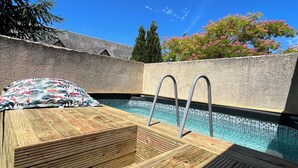 Een houten terras met een zwembad, metalen trappen en een stenen muur.