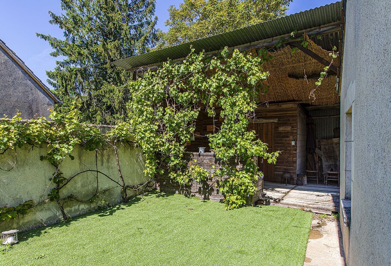 Une cabane en bois avec un toit de chaume, une pelouse bien entretenue et un mur en pierre.