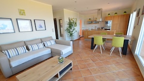 A modern living room with a sofa, coffee table, and a dining area with chairs and a table.