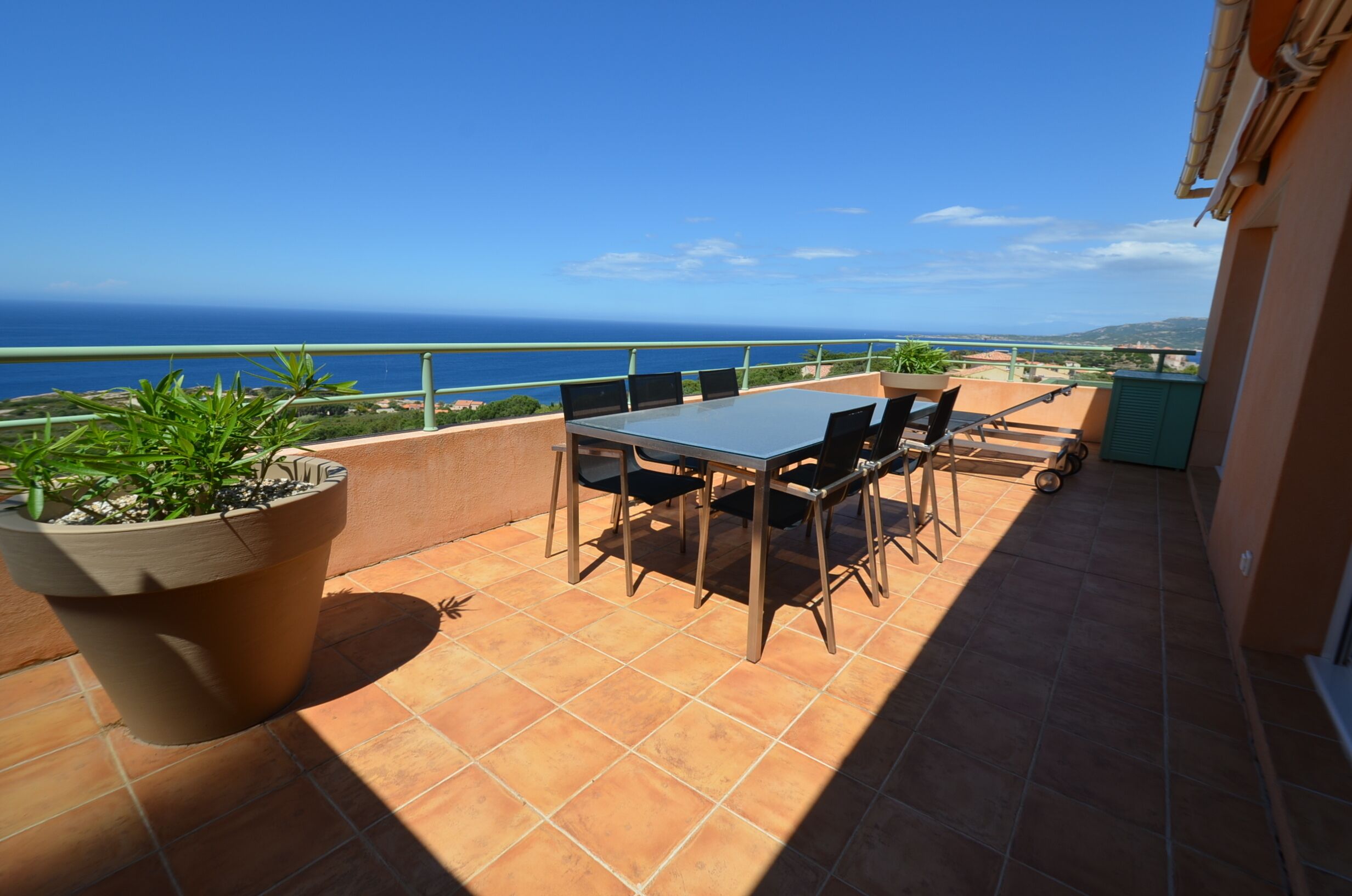 A terrace with a table and chairs, a potted plant, and a view of the ocean.