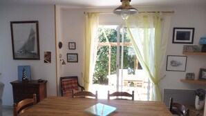 Un coin repas avec une table en bois, des chaises et une table avec un plateau en verre. Les murs sont ornés de tableaux encadrés et il y a une fenêtre avec des rideaux.