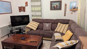 Un salon avec un canapé marron, des coussins à rayures, une table basse en bois, un téléviseur à écran plat et une carte accrochée au mur.