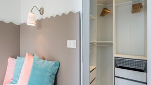 Ein Schlafzimmer mit einem Bett, einem Nachttisch, einer Wandlampe und einem Kleiderschrank mit Kleidung.
