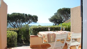 Un patio con mesa y sillas, vista al mar y algo de vegetación.