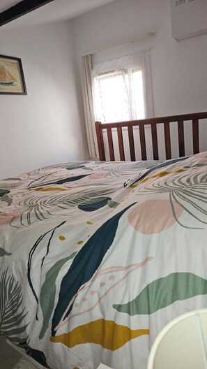 A bedroom with a bed, a window with curtains, and a framed picture on the wall.