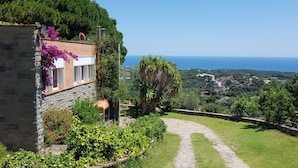 Un edificio de piedra con jardín, un camino de piedra y vista al mar.