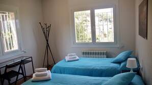 Un dormitorio con dos camas, un radiador, una silla y una ventana con vistas a la vegetación.