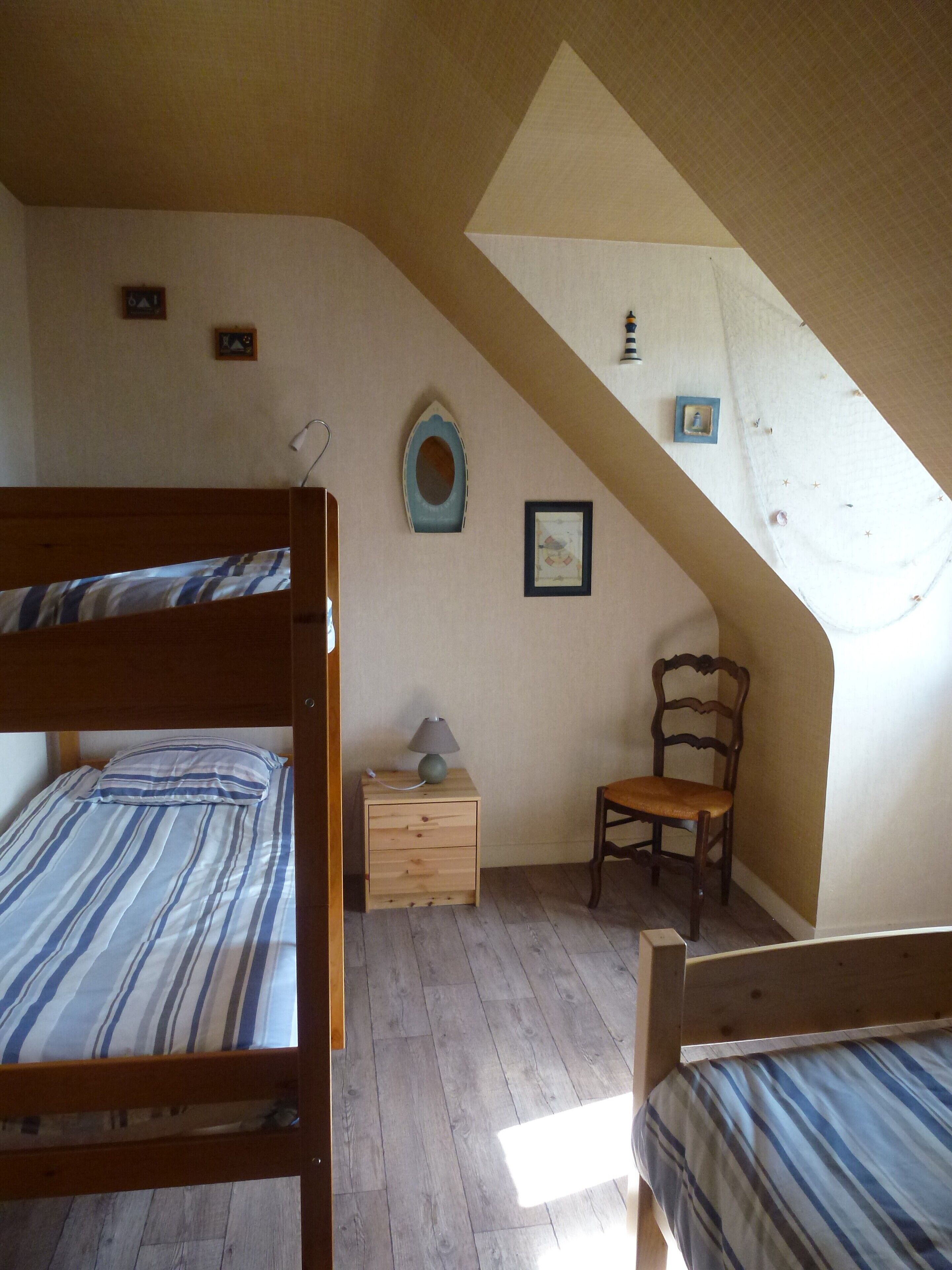 Une chambre avec un plafond en pente, un lit en bois, une table de chevet, une chaise et une petite table avec une lampe.