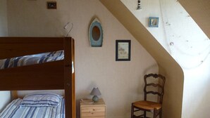 A bedroom with a sloped ceiling, a wooden bed, a nightstand, a chair, and a small table with a lamp. - South Brittany House Sea View in Port-louis 8 -10 people (Port-Louis)