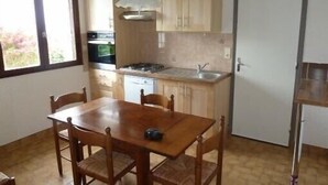 A compact kitchen with wooden cabinets, a gas stove, and a dining table with chairs. - South Brittany House Sea View in Port-louis 8 -10 people (Port-Louis)