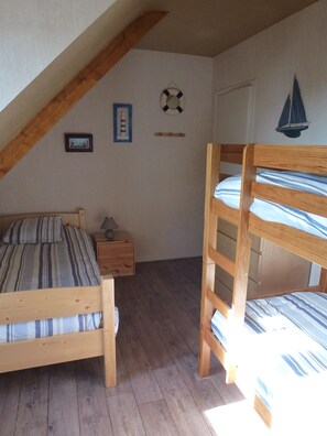 A bedroom with two bunk beds, a wooden nightstand, a framed picture, a life preserver decoration, and a sailboat decoration on the wall.